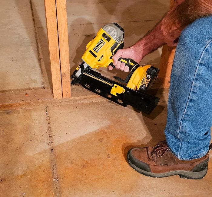 Entrepreneur en bâtiment utilisant une cloueuse sans fil DeWalt pour fixer le goujon à la plaque inférieure.