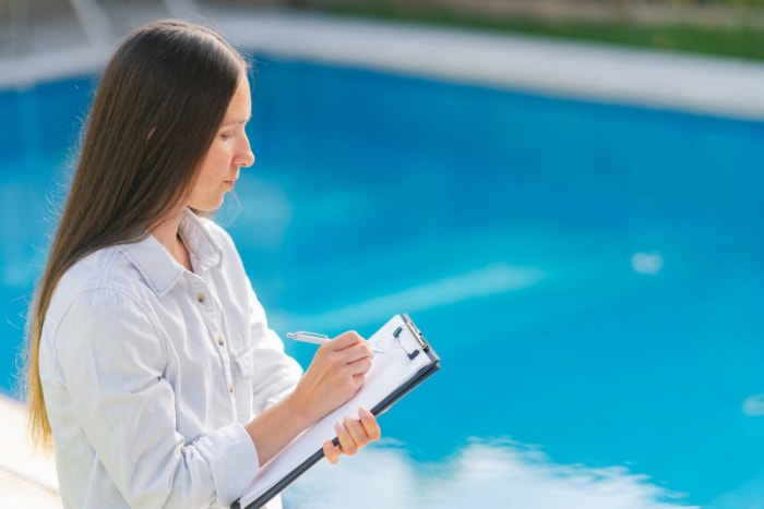 Une personne vérifie les éléments d’une liste lors de l’évaluation d’une piscine.