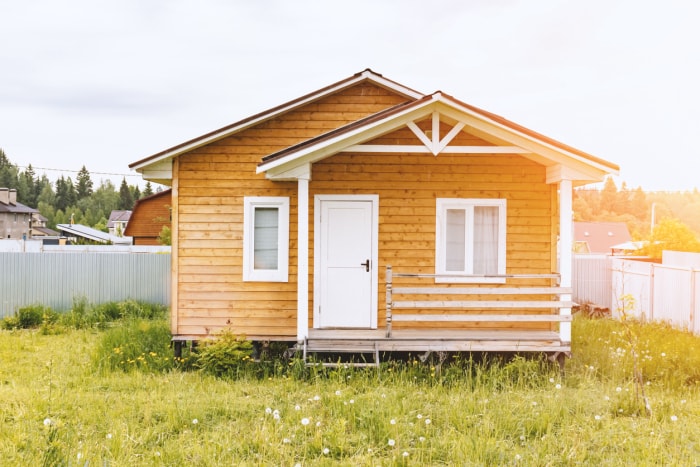 Petite maison à ossature bois avec terrasse et fenêtres et porte blanches comme résidence de campagne lors d'une journée d'été ensoleillée.