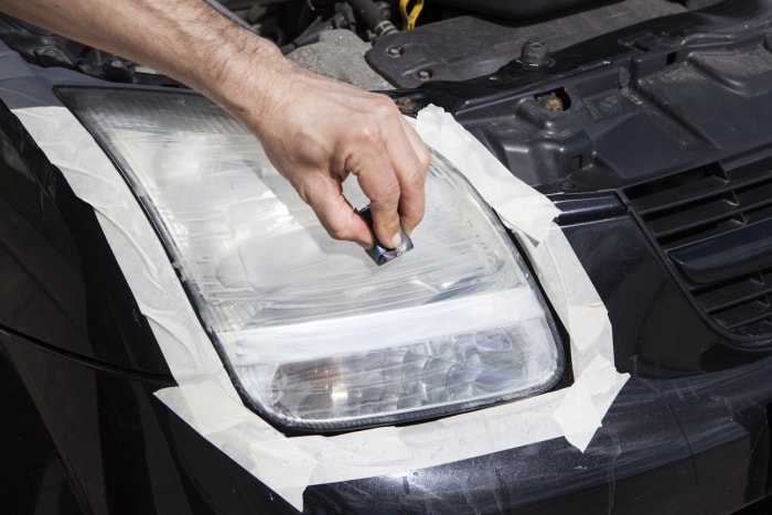 Application manuelle des matériaux du kit de phares sur le phare passager d'une voiture noire