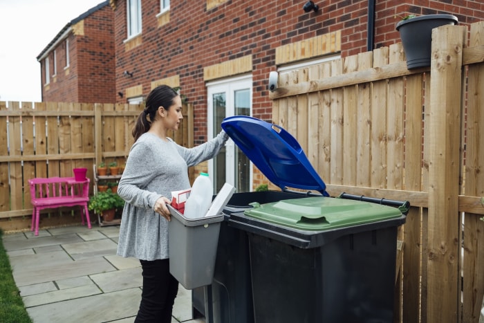 Une personne qui met des contenants en plastique et en carton dans un bac de recyclage dans l’arrière-cour.