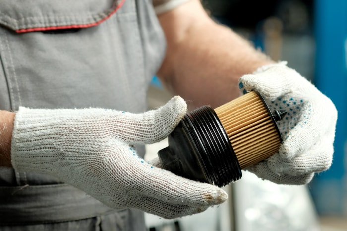 mécanicien portant des gants et tenant un filtre à carburant