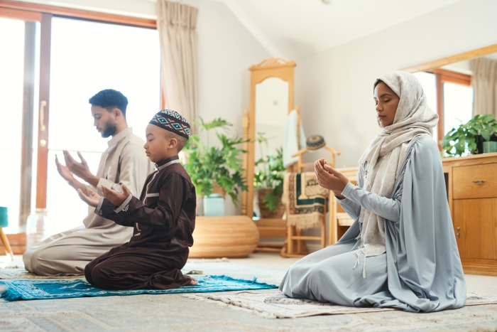 Vue d'un jeune couple musulman et de leur fils priant dans le salon de leur maison.