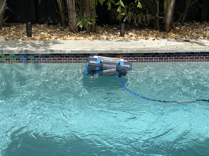 Robot nettoyeur de piscine Dolphin Premier se déplaçant dans la piscine avec la terrasse et le paysage rocheux