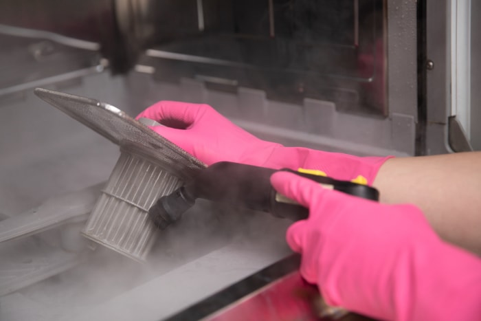 Mains gantées pour nettoyer le filtre du lave-vaisselle avec un nettoyeur à vapeur chaude.