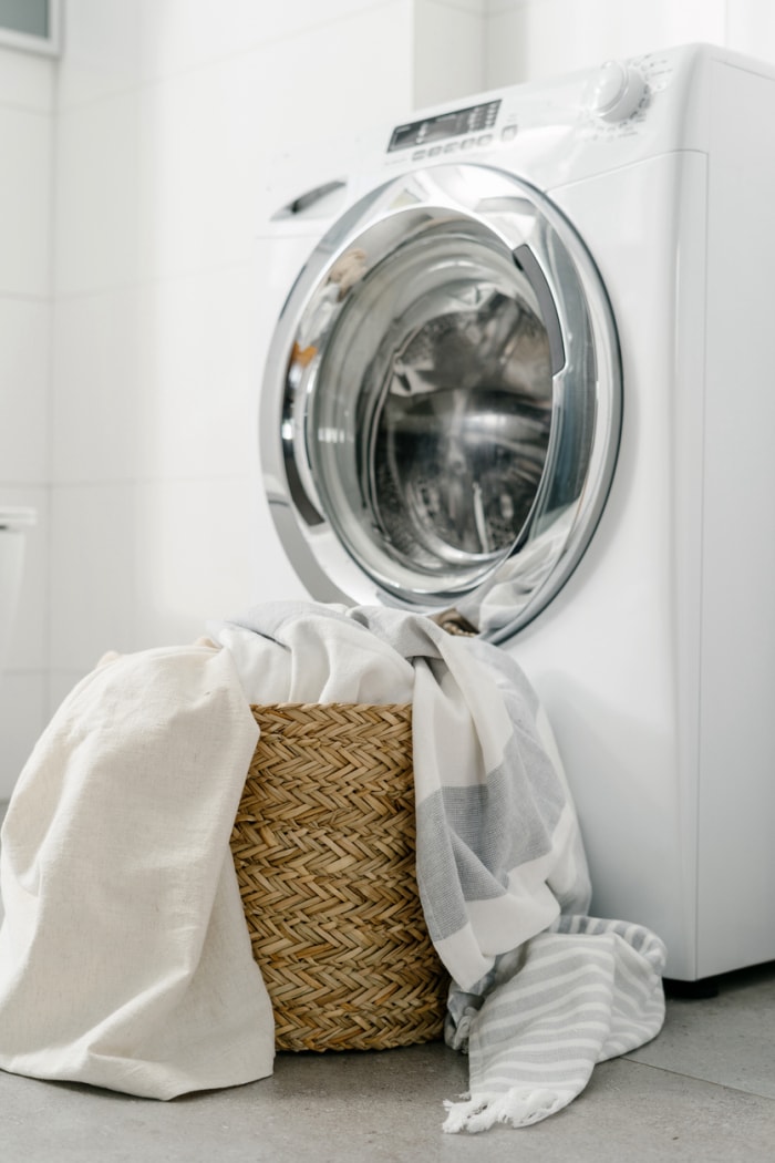 draps blancs et gris dans un panier en osier posé devant la machine à laver