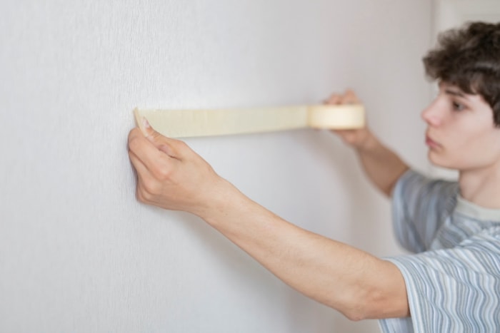 Jeune homme tenant du ruban adhésif de peintre contre un mur.