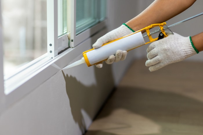 Une personne portant des gants de construction scelle une fenêtre avec du mastic.