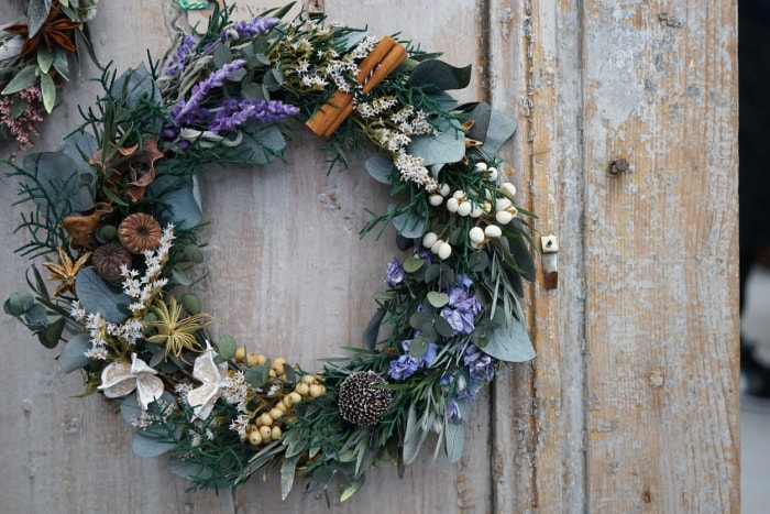 Couronne d'hiver avec des bâtons de lavande et de cannelle, et des fleurs sur une porte patinée.