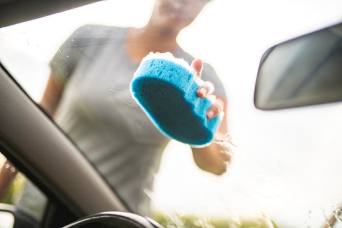 Personne frottant la vitre d'une voiture avec une éponge.