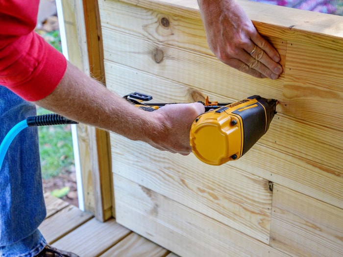 Une personne utilisant le cloueur de finition à angle sans fil DeWalt 20V MAX XR 16 GA pour fixer des panneaux dans un porche.