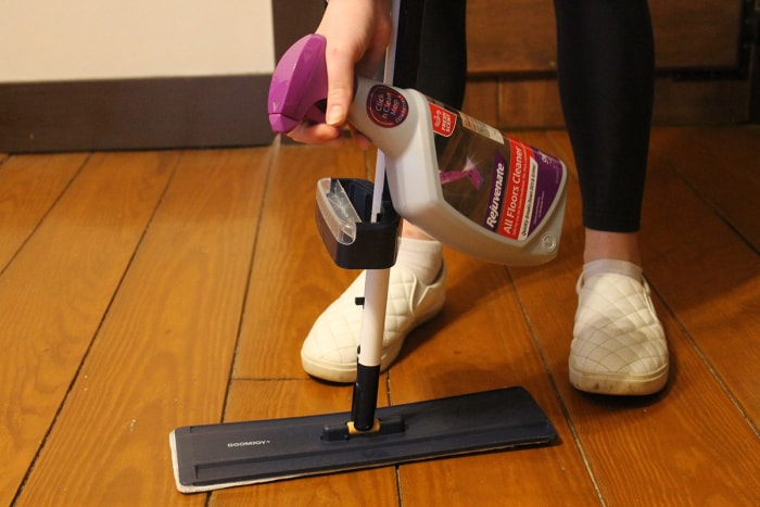 Une personne pulvérisant un plancher en bois avec le nettoyant pour tous les sols Rejuvenate avant de passer la serpillère.