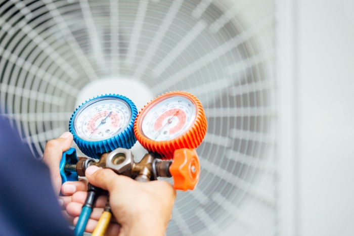 Un technicien en climatisation utilise un outil de jauge pour tester un climatiseur extérieur.