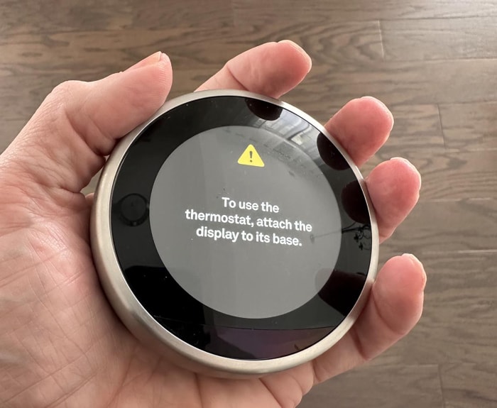 Une personne tenant le thermostat Google Nest Learning pendant les tests, qui est suffisamment petit pour tenir dans la paume de sa main.