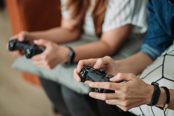 Gros plan des mains de deux jeunes tenant des manettes de jeux vidéo.