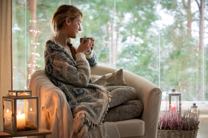 Jeune femme assise près de la fenêtre avec une boisson chaude.