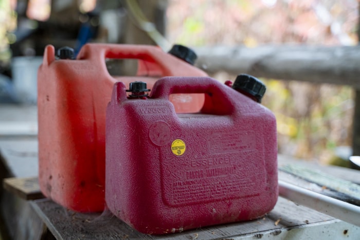 Deux jerrycans rouges contenant du diesel sont posés l'un à côté de l'autre sur une table en bois à l'extérieur.