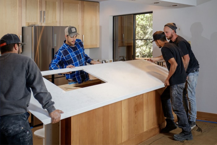 Une équipe d'ouvriers place un comptoir en quartz sur une base d'armoire en bois dans une cuisine.