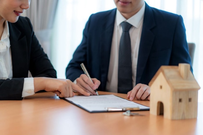 Deux personnes sont assises à une table et examinent des documents tandis qu'une petite maquette de maison est posée sur la table. 