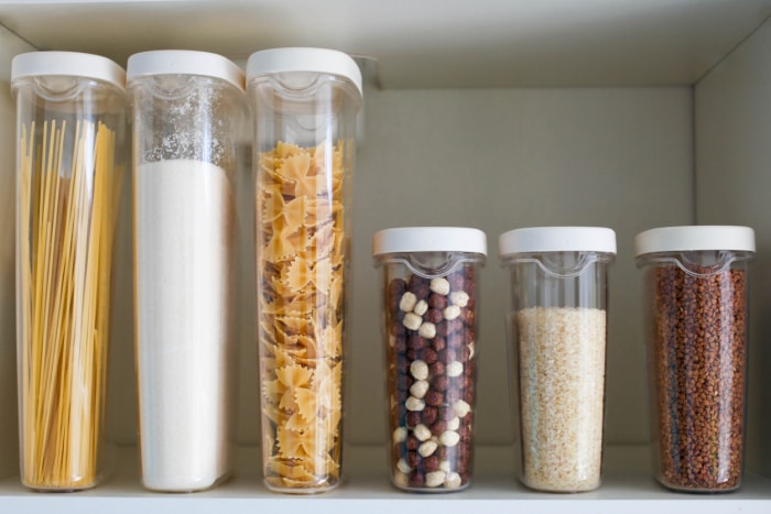 Un garde-manger avec des pâtes, du sucre, des noix et du riz organisés dans des contenants en plastique.