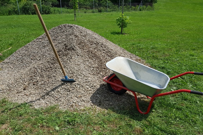 Pelle de brouette de chantier sur un tas de cailloux dans un jardin.