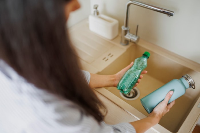 Femme tenant une bouteille en plastique dans une main et une bouteille réutilisable dans l'autre