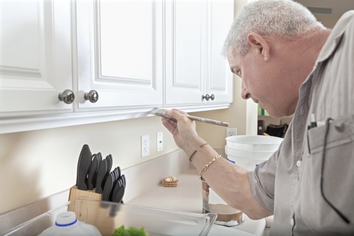 Un homme mûr peint les armoires de cuisine en blanc.