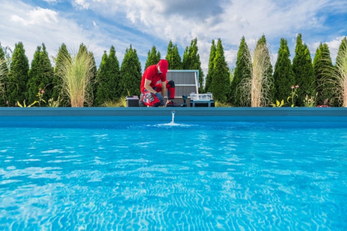 Un ouvrier nettoie une piscine par une journée lumineuse et ensoleillée.