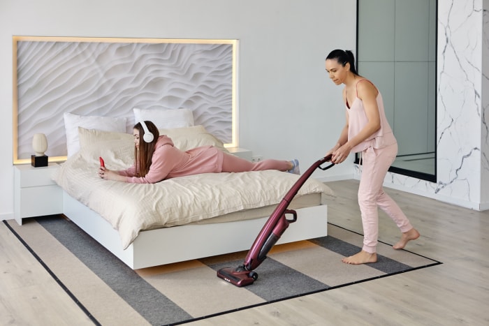 Une personne utilisant le meilleur aspirateur bon marché pour nettoyer un tapis sous un lit sur lequel se trouve une autre personne.