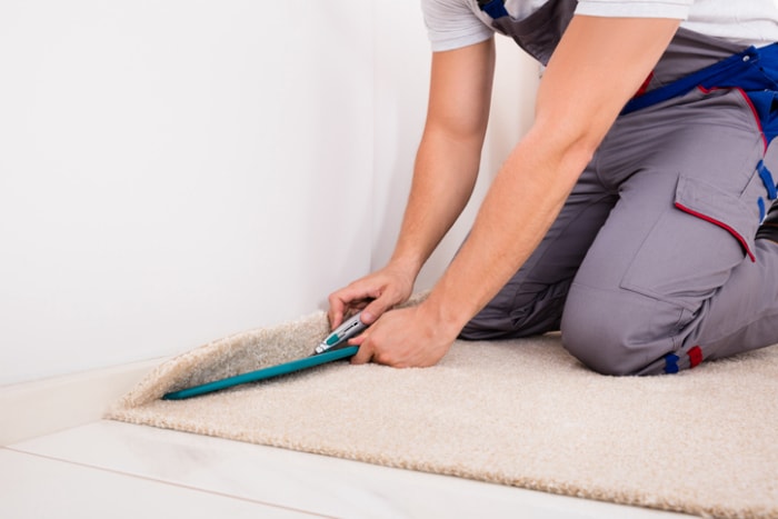 homme-en-gris-sur-mesure-installe-la-moquette-en-l'alignant-sur-la-planche-d'un-plancher-blanc