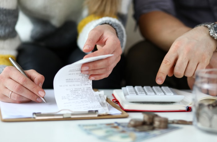 Gros plan sur les mains de deux personnes qui consultent des documents et utilisent une calculatrice. 