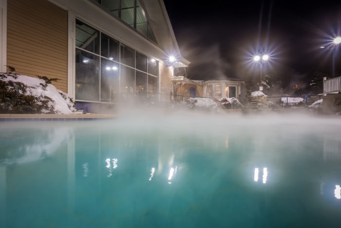 De la vapeur s'échappe du haut d'une piscine, la nuit, dans un jardin enneigé.