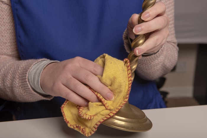 Femme avec un pull bleu polissant des bougeoirs en laiton avec un chiffon jaune.