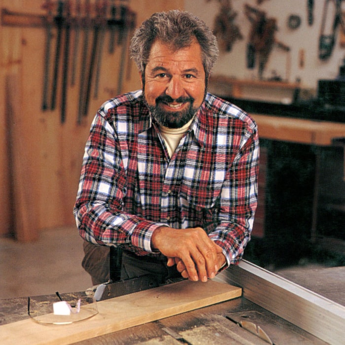 Bob Vila, vêtu d'une chemise à carreaux, se penche en avant dans un atelier de menuiserie.