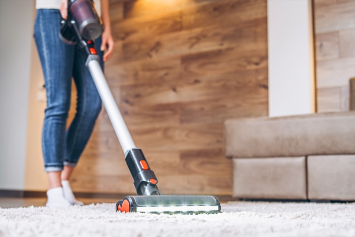 vue au niveau du sol d'une femme passant l'aspirateur sur un tapis dans le salon