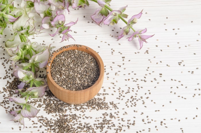 Graines de chia, un super aliment sain avec une fleur sur fond de bois blanc. Salvia hispanica.