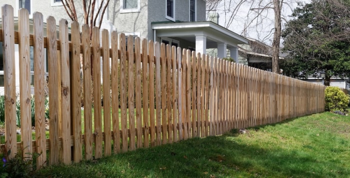 Une clôture en bois en forme d'oreille de chien borde la cour avant d'une maison de quartier.