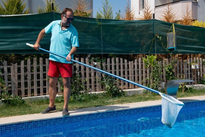 Un homme utilise un filet pour nettoyer une piscine.