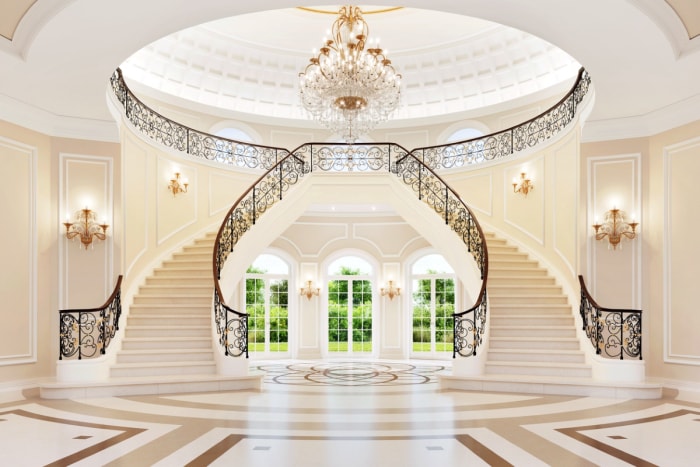 Un double escalier blanc domine le grand hall d'entrée d'une maison de maître lumineuse.