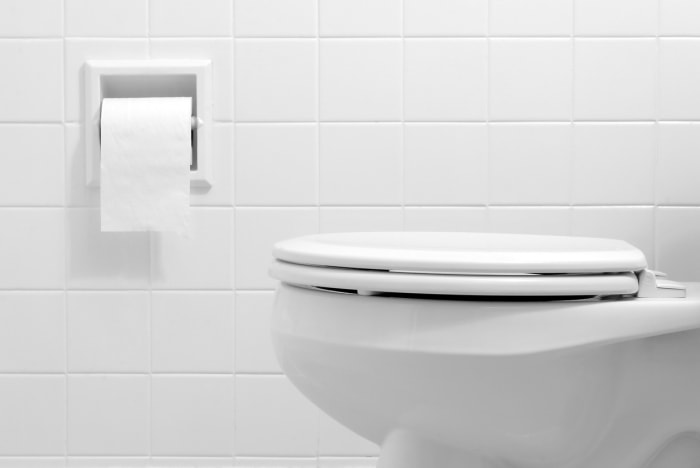 A white bathroom with a closed toilet next to toilet paper.