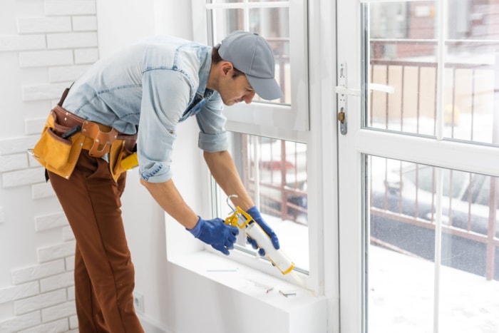 Un bricoleur termine l'installation d'une fenêtre avec du calfeutrage.