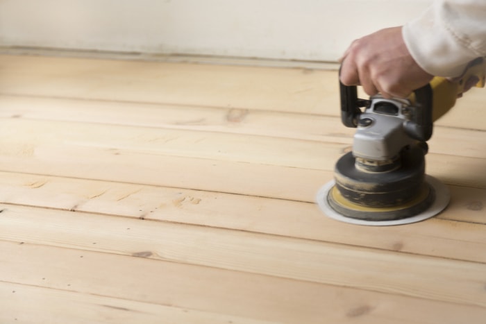 L'homme utilise une ponceuse orbitale aléatoire pour poncer un parquet de couleur claire.