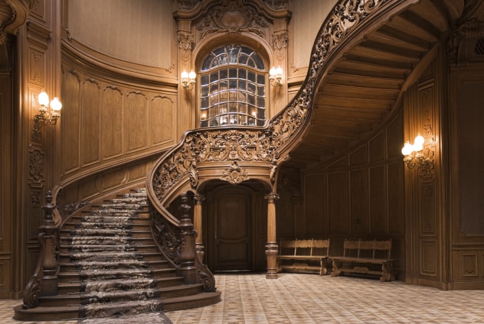 Un escalier en bois sculpté de manière élaborée serpente dans un hall d'entrée lambrissé de bois.