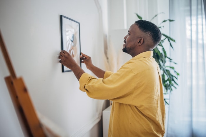 Un homme accroche un tableau encadré sur le mur du salon.