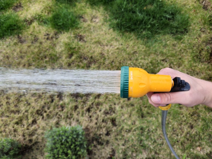 Gros plan d'une main tenant un arroseur jaune arrosant de l'herbe sèche