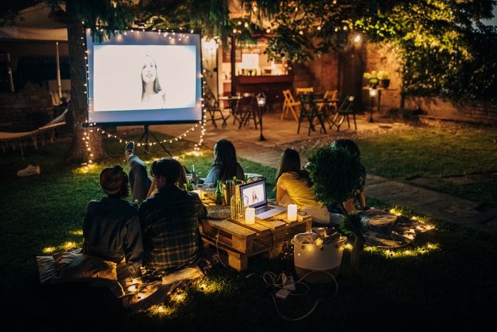 Des amis regardent un film sur le vidéoprojecteur dans le jardin