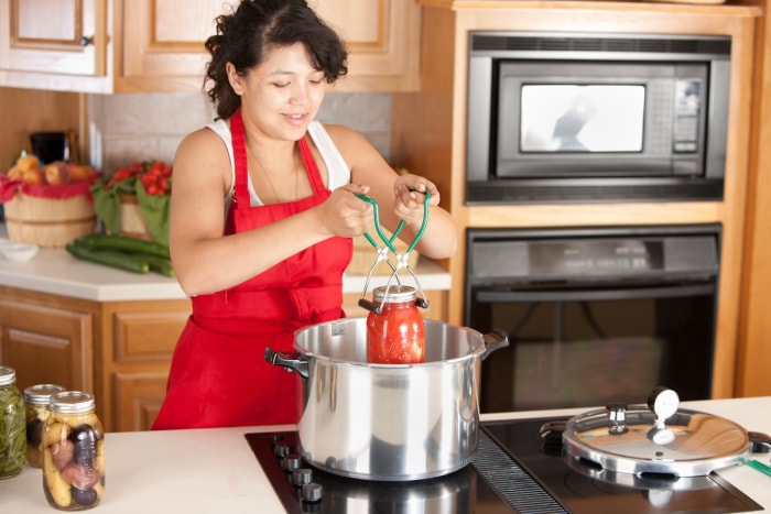 Une femme en tablier met des tomates en conserve.