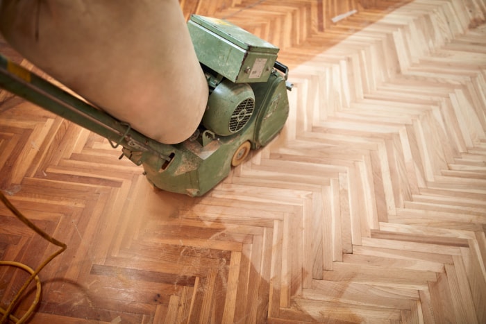 Une ponceuse est utilisée pour poncer un parquet à chevrons.