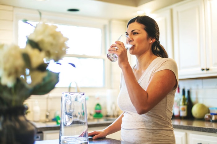 Femme buvant de l'eau dans un verre à son domicile.