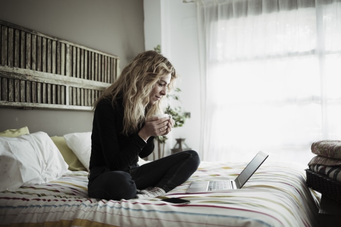 Femme utilisant un ordinateur portable assise sur son lit à la maison